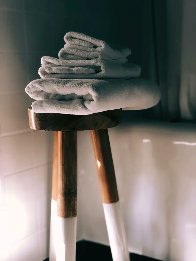 Serviettes blanches pliées sur un tabouret en bois, ambiance hammam feutrée