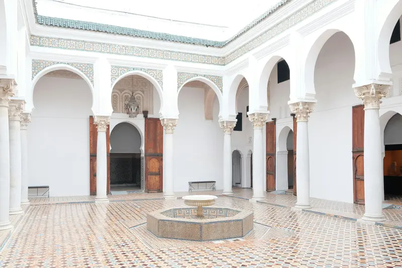 Cour intérieure marocaine aux arcades blanches sculptées et sol en zellige, fontaine centrale