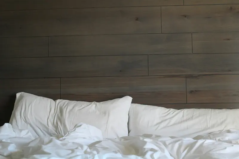 Housse de couette blanche moelleuse sur un lit, mur en bois sombre en arrière-plan