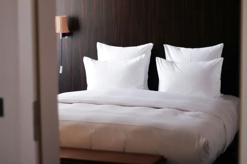 Lit d'hôtel avec oreillers blancs gonflés et drap tendu, ambiance chaleureuse